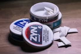 Nicotine pouches placed next to Zyn snus cans on a clean surface
